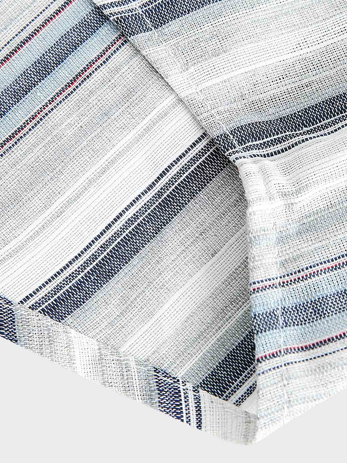 「シャツ裾のワインレッドの刺繍タグのクローズアップ。繊細さとおしゃれさを演出。」