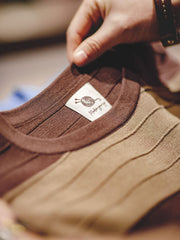 カラーブロック3Dストライプニット短袖Tシャツのクローズアップ。細部にわたる先進的な編み技術による立体的ストライプが、クラシックなデザインにモダンなひねりを加えています。