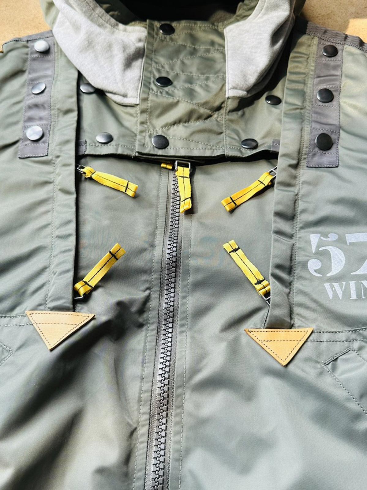 製品画像:57飛行隊機能性MA-1フライトジャケットの正面展示。取り外し可能なフード付きのミリタリー風ジャケット。
詳細画像:取り外し可能なフードと多機能ポケットのディテール。収納力と実用性を兼ね備えたデザイン。