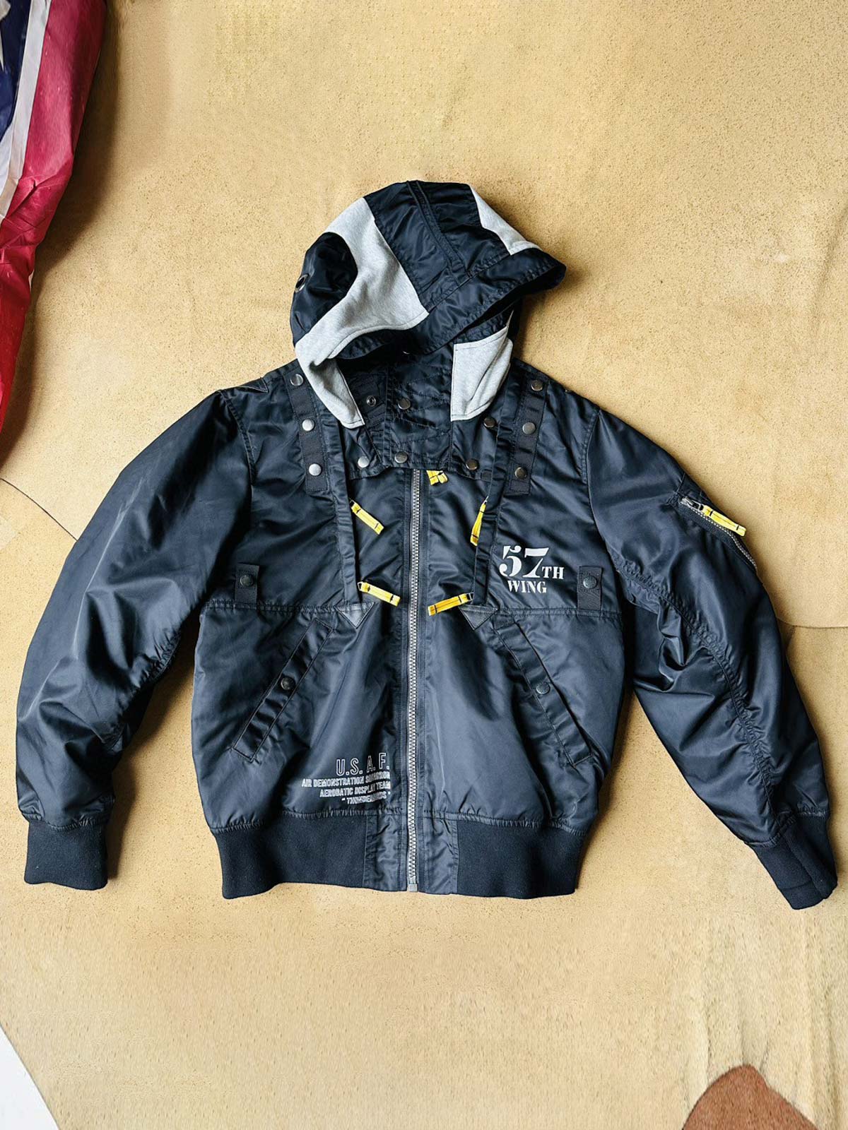 製品画像:57飛行隊機能性MA-1フライトジャケットの正面展示。取り外し可能なフード付きのミリタリー風ジャケット。
詳細画像:取り外し可能なフードと多機能ポケットのディテール。収納力と実用性を兼ね備えたデザイン。