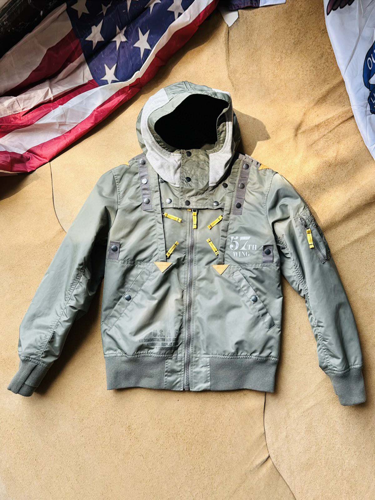 製品画像:57飛行隊機能性MA-1フライトジャケットの正面展示。取り外し可能なフード付きのミリタリー風ジャケット。
詳細画像:取り外し可能なフードと多機能ポケットのディテール。収納力と実用性を兼ね備えたデザイン。