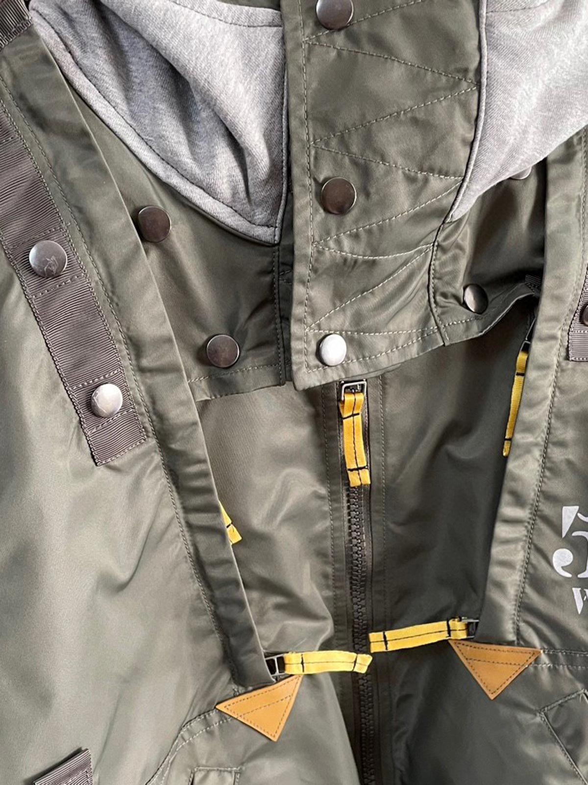 製品画像:57飛行隊機能性MA-1フライトジャケットの正面展示。取り外し可能なフード付きのミリタリー風ジャケット。
詳細画像:取り外し可能なフードと多機能ポケットのディテール。収納力と実用性を兼ね備えたデザイン。