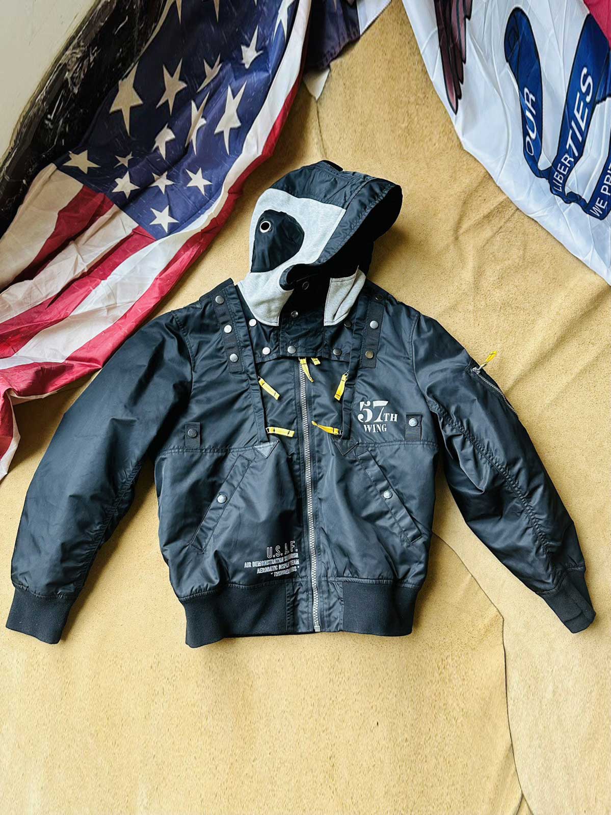 製品画像:57飛行隊機能性MA-1フライトジャケットの正面展示。取り外し可能なフード付きのミリタリー風ジャケット。
詳細画像:取り外し可能なフードと多機能ポケットのディテール。収納力と実用性を兼ね備えたデザイン。