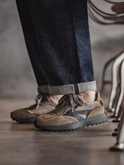 モデルがスモークオリーブ色クラシック70年代ジョギングシューズを着用し、スタイリッシュなカジュアルコーディネートを示す