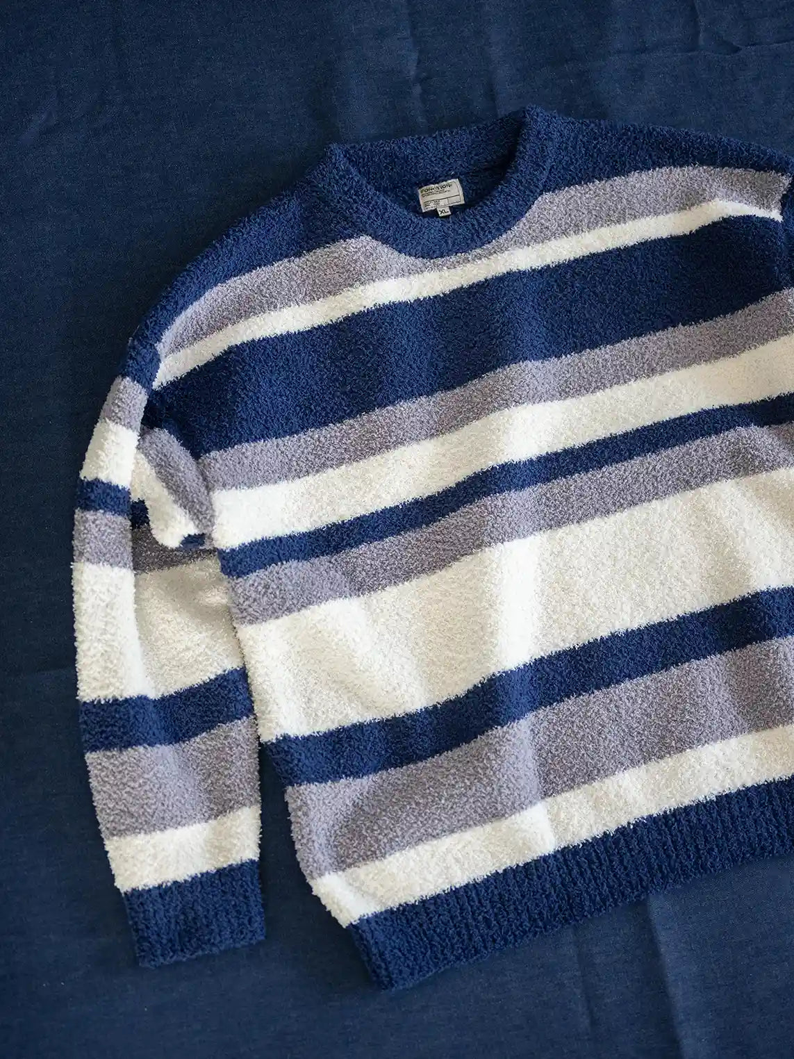 短丈ワイドシルエットのストライプニット、微起毛感のある半边フリース素材。詳細画像:袖口・裾のリブ仕様やブルー系/ブラウン系の不規則ストライプ。モデル画像:モデルがレイヤードスタイルで着用し、レトロモダンな雰囲気を演出。