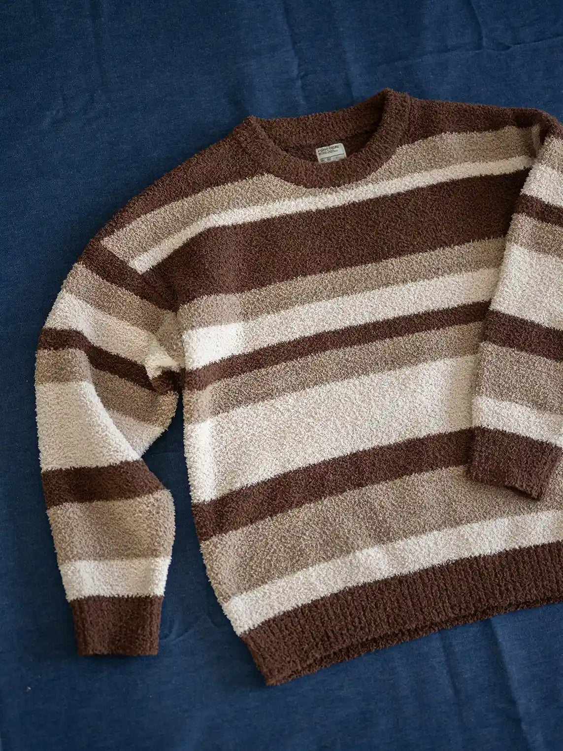 短丈ワイドシルエットのストライプニット、微起毛感のある半边フリース素材。詳細画像:袖口・裾のリブ仕様やブルー系/ブラウン系の不規則ストライプ。モデル画像:モデルがレイヤードスタイルで着用し、レトロモダンな雰囲気を演出。