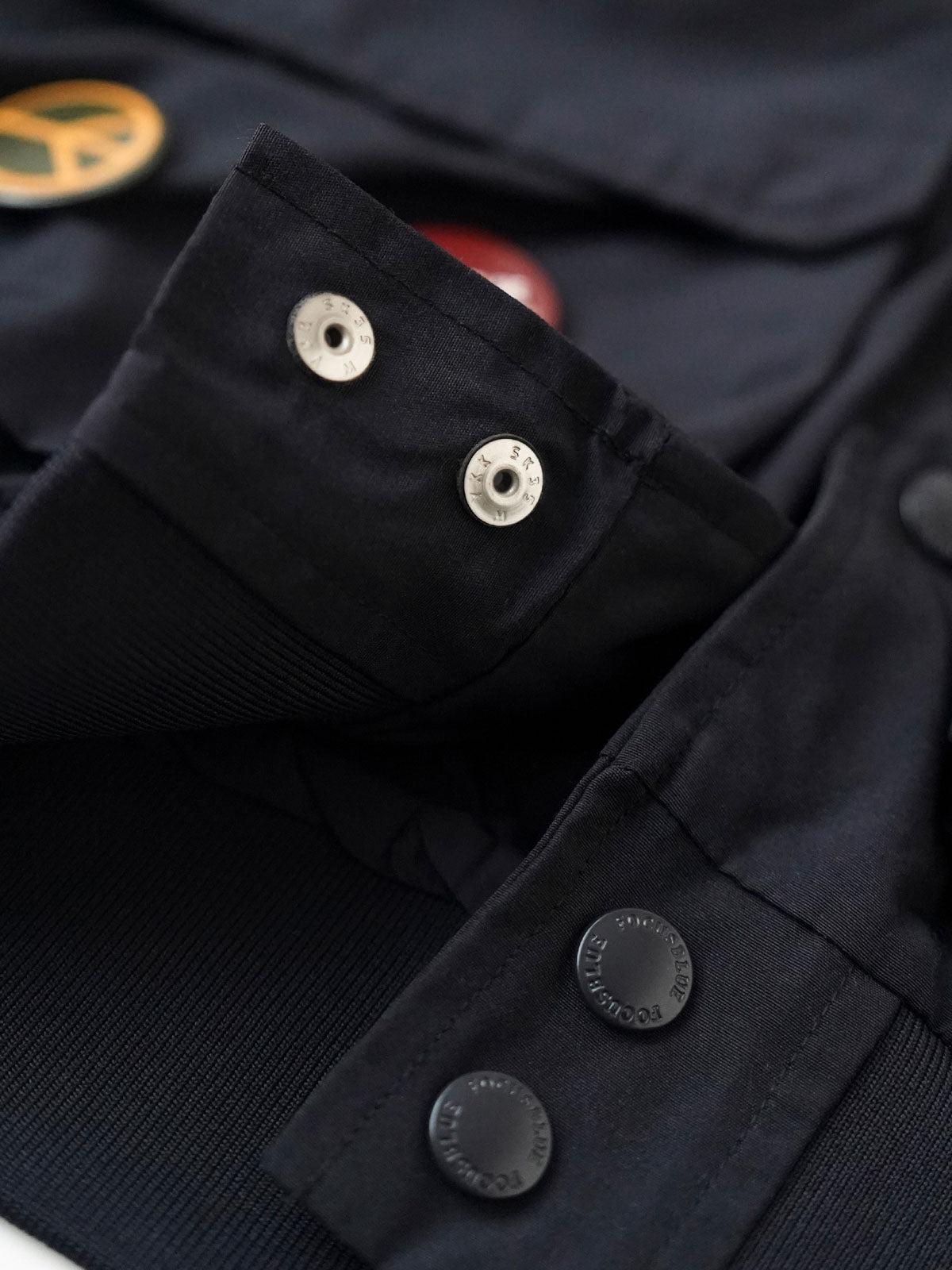 製品画像
「アシンメトリーデザインの多ポケットキャンプワークジャケット全体の展示図。クラシックなフィッシングジャケットとワークスタイルが融合したデザインで、ユニークなアシンメトリーデザインが実用性と個性を強調。防撥水機能を備えたポリエステルとコットン混紡生地を使用し、快適な着心地を提供します。」
詳細画像
「胸元のロゴ刺繍とアシンメトリーな多機能ポケットのディテール特写。YKKカスタムジッパーとロゴ入りスナップボタンが、高品質のディテールを引き立て、機能性とスタイルを両立させています。ダブルレイヤーのリブ編みが施され、袖口と裾のフィット感と耐久性を向上させています。」