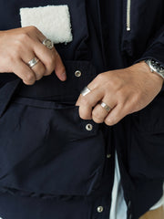 詳細画像
「胸元のロゴ刺繍とアシンメトリーな多機能ポケットのディテール特写。YKKカスタムジッパーとロゴ入りスナップボタンが、高品質のディテールを引き立て、機能性とスタイルを両立させています。ダブルレイヤーのリブ編みが施され、袖口と裾のフィット感と耐久性を向上させています。」
モデル画像
「モデルがアシンメトリーデザインの多ポケットキャンプワークジャケットを着用し、アウトドアシーンでのコーディネートを披露。ショート丈のルーズフィットシルエットが、カジュアルな日常コーディネートやアウトドア活動に最適なスタイルを提供します。」