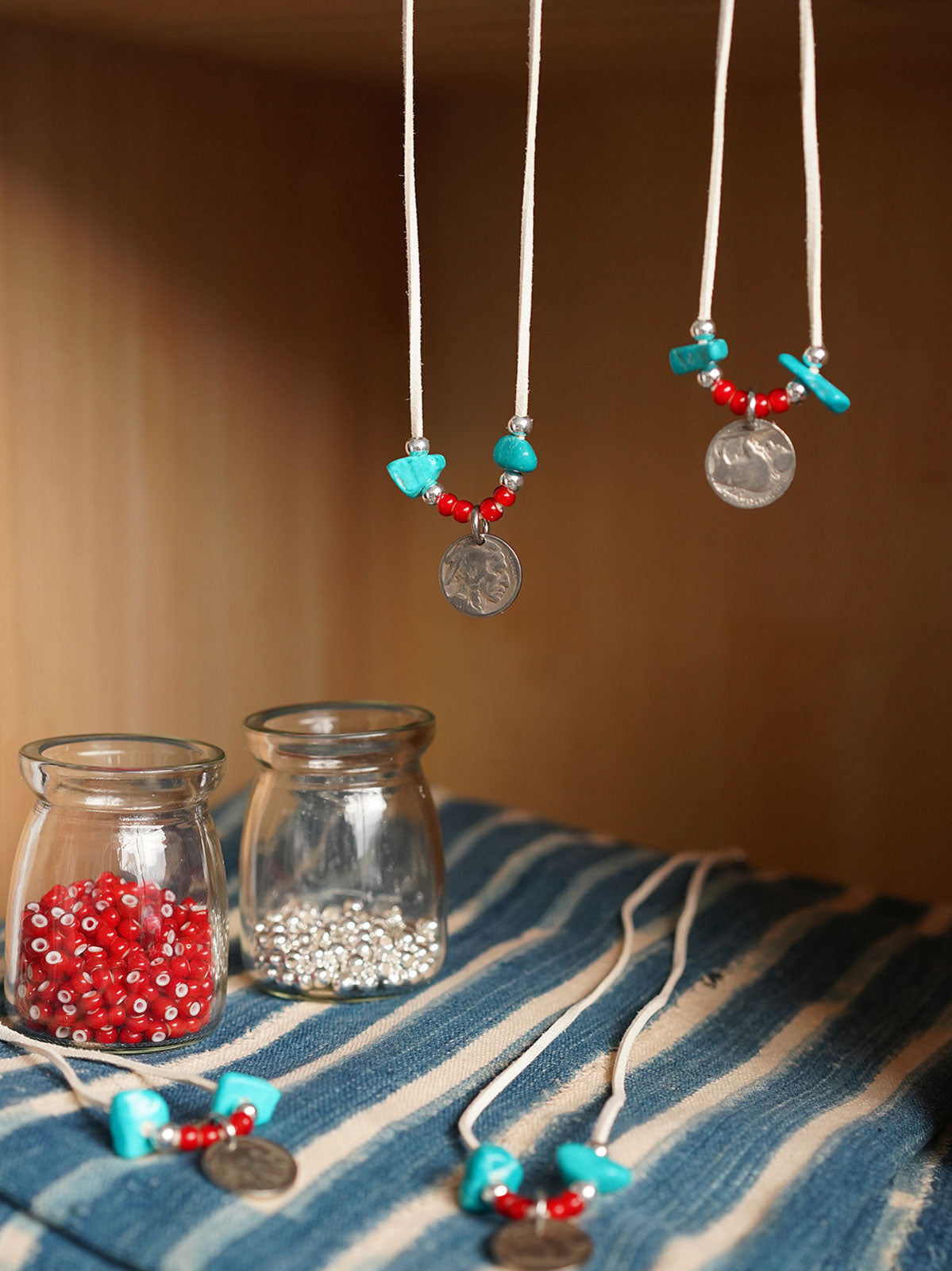 製品画像
「ハンドメイドインディアンコインネックレスの全体展示図。天然ターコイズ、アンティークガラスビーズ、アメリカの5セント硬貨を組み合わせたヴィンテージ感漂うデザインが特徴。」
詳細画像
「天然ターコイズとアンティークガラスビーズのディテール特写。各ビーズと硬貨が手作りで、個性あふれる美しさを際立たせています。」