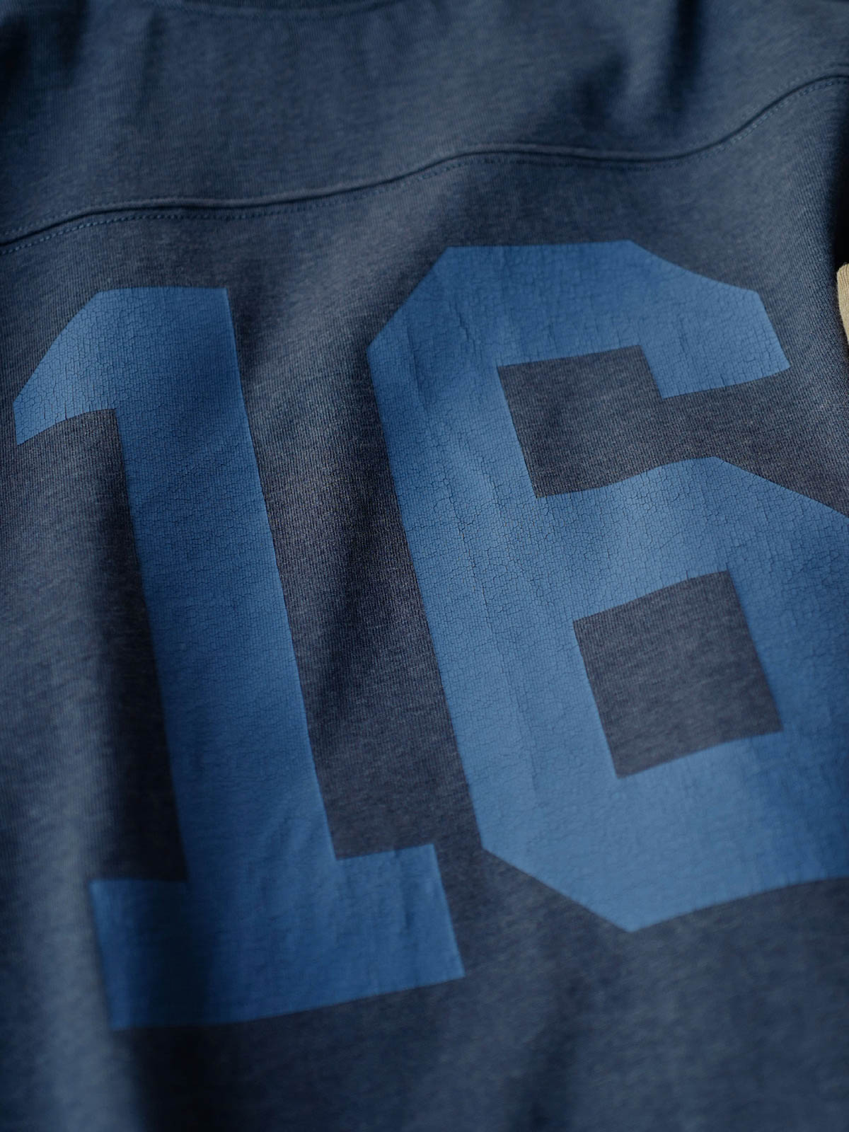 製品画像: ヴィンテージ感漂う杢調ラグビー長袖Tシャツの全体像を正面から撮影した画像
詳細画像: クラシックなひび割れ風ナンバープリントとドロップショルダーのディテールをクローズアップした画像