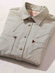 製品画像: アイボリー色のスナップボタン付きストライプシャツの正面図。ヴィンテージウエスタンデザインが特徴。
詳細画像: シャツの肩部ディテールとトライアングルレザー補強部分のクローズアップ。ダブルステッチと色織り生地が耐久性とスタイルを強調。