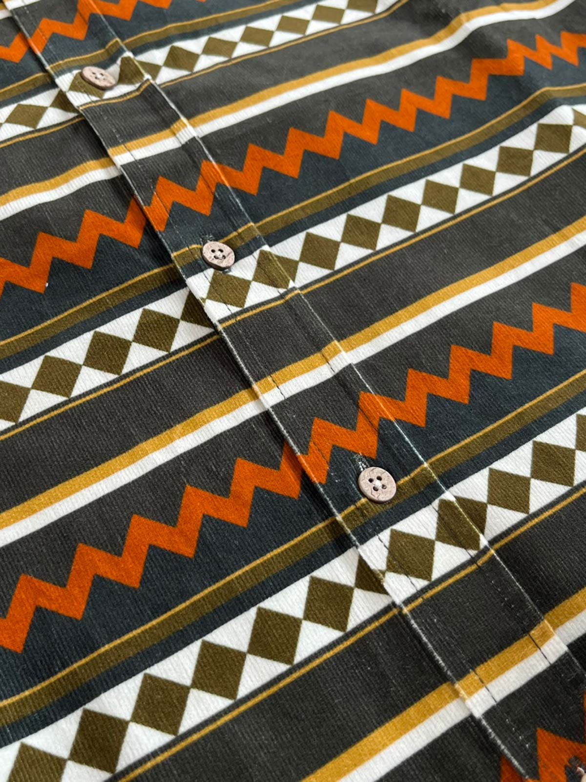 製品画像: ヴィンテージコーデュロイワイドカラー長袖シャツの正面画像。厚手のコーデュロイ素材で、快適な着心地を実現。
詳細画像: コーデュロイ素材のリブディテールとヴィンテージプリントの特写。