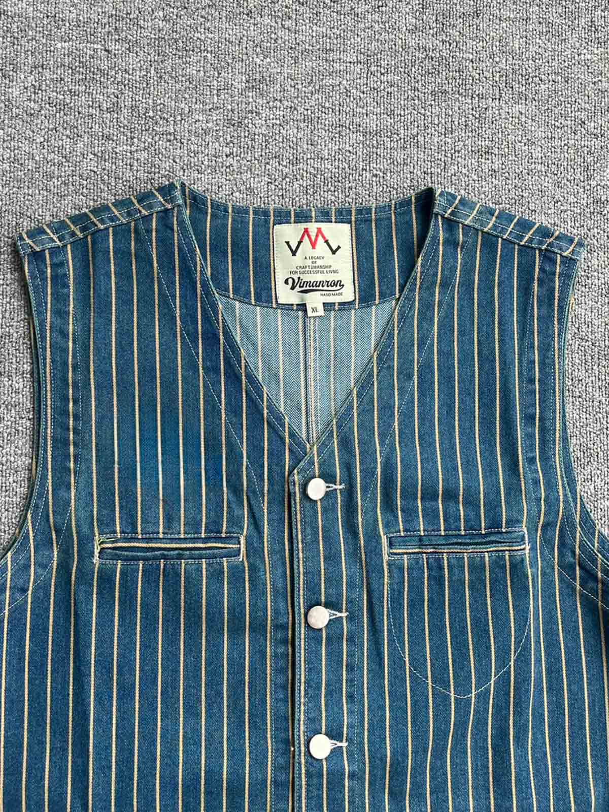 製品画像: アメリカンワークスタイルのデニムストライプベストの正面ビュー。Vネックとスリムフィットデザインが特徴。100%コットン素材の詳細が見える。
詳細画像: デニムストライプ素材のクローズアップとVネックデザインのディテール。生地の質感と縫製がよくわかる。