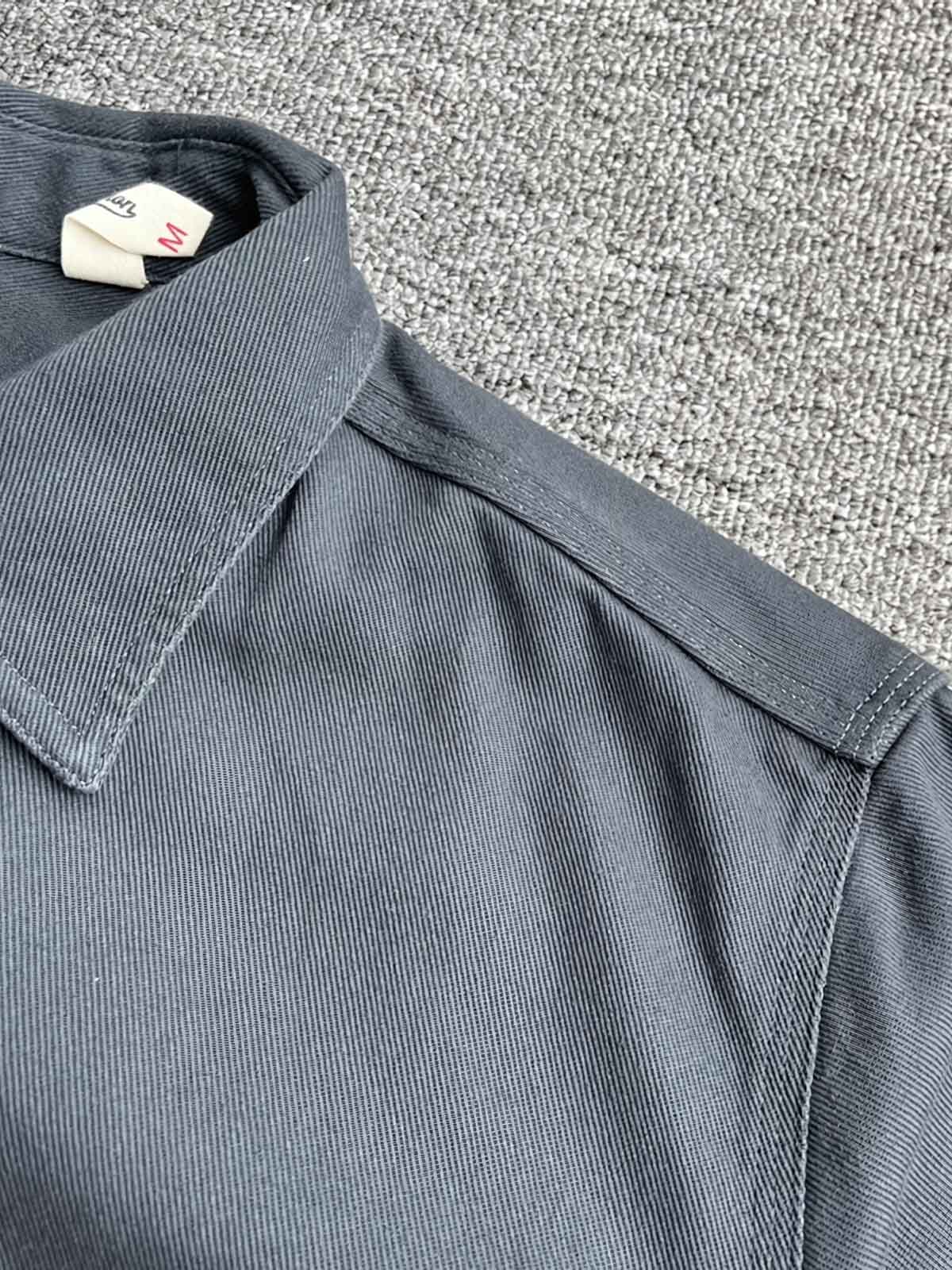 製品画像: クラシックなツイル生地の長袖ワークシャツの正面画像。100%コットン素材で作られた耐久性のあるシャツで、レトロなワークユニフォームスタイルを再現。
詳細画像: 高品質なツイル生地の長袖ワークシャツのディテール画像。細やかな縫製とコットンツイル素材の耐摩耗性が強調された画像。クラシックなワークスタイルの要素が確認できるクローズアップショット。