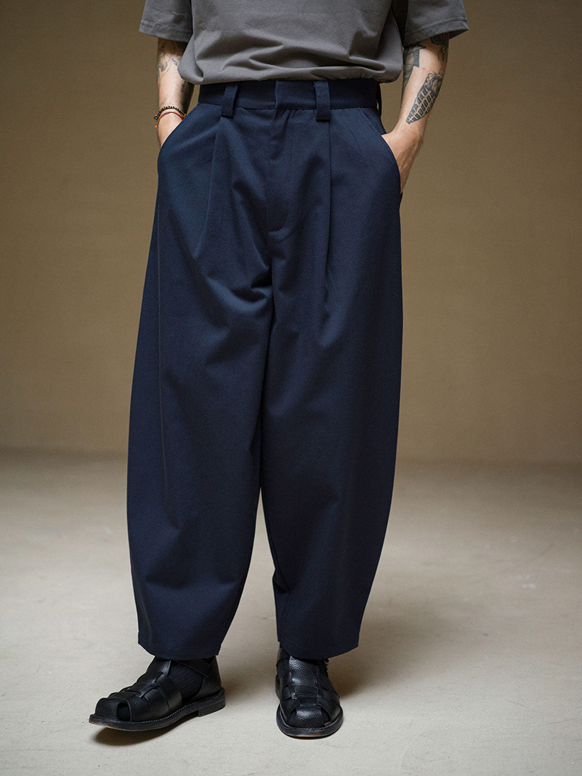 詳細画像: ツイル素材のディテールとプリーツが特徴のパンツ、シンプルなデザインで幅広いシーンに対応
モデル画像: モデルが着用する立体裁断シングルプリーツパンツ、テーパードデザインで美しいシルエットを演出