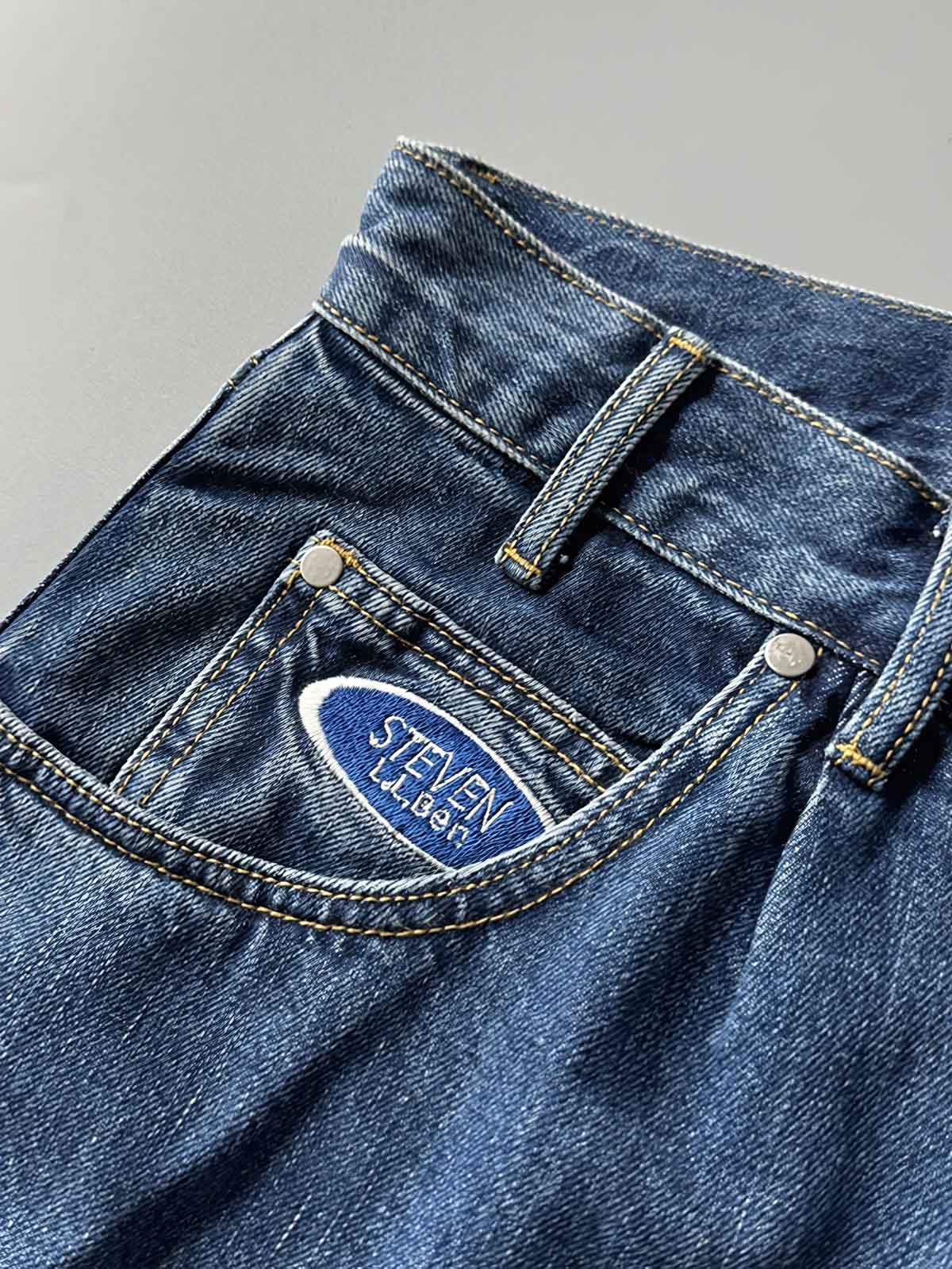 製品画像: 刺繍デザインが特徴のテーパードシルエットデニムパンツ全体画像
詳細画像: ポケット部分の刺繍ディテールとクラシックデニムブルーの生地