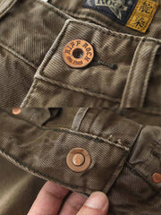 製品画像:アメカジ風泥染めストレートデニムパンツの正面展示。低彩度のブラウンカラーがヴィンテージ感を演出。
詳細画像:カスタムボタンとウォッシュ加工のディテールをクローズアップ。レザーパッチがデザインのアクセントに。