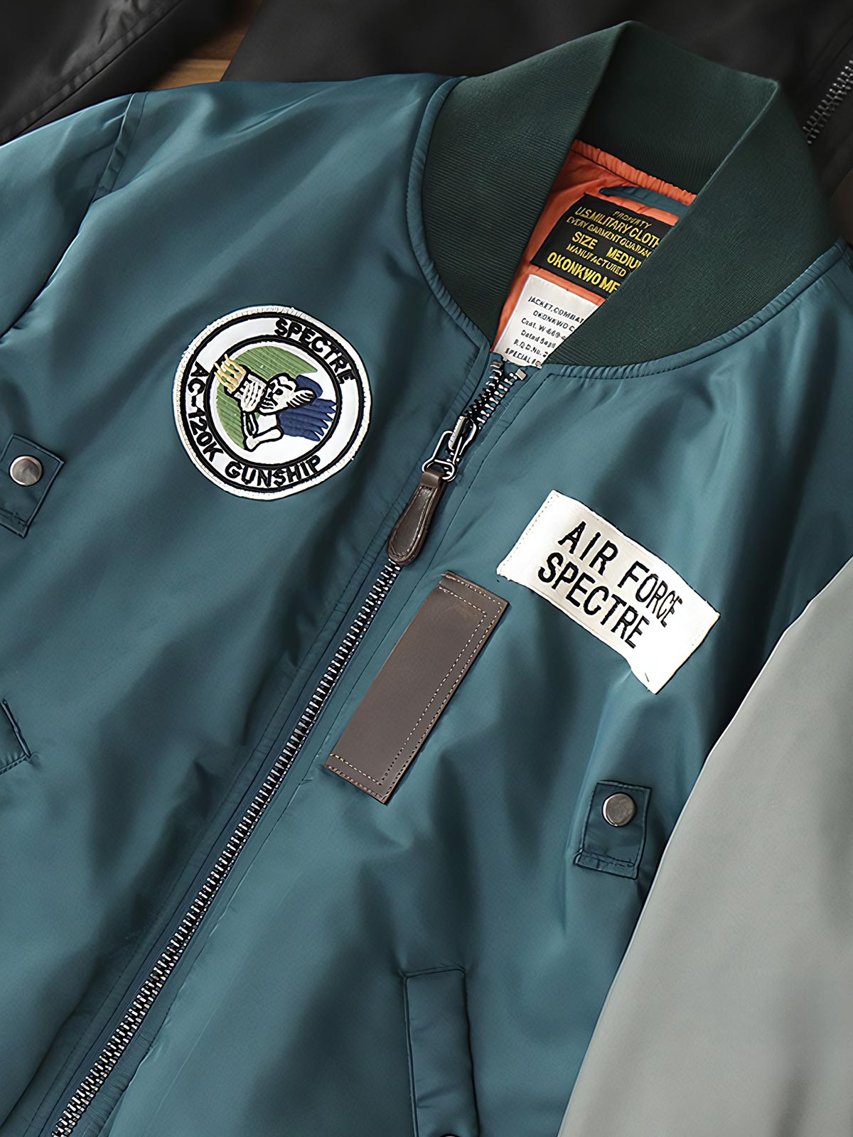 製品画像:ヴィンテージMA-1フライトジャケットの正面図。防水ナイロン素材とオレンジ色の裏地、刺繍バッジが特徴的なデザイン。
詳細画像:刺繍バッジと識別テープ、ジッパーのディテールをクローズアップした画像。ミリタリーウェアの本格的なスタイルを強調。