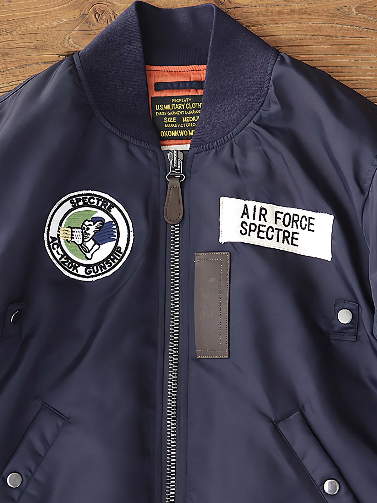 製品画像:ヴィンテージMA-1フライトジャケットの正面図。防水ナイロン素材とオレンジ色の裏地、刺繍バッジが特徴的なデザイン。
詳細画像:刺繍バッジと識別テープ、ジッパーのディテールをクローズアップした画像。ミリタリーウェアの本格的なスタイルを強調。