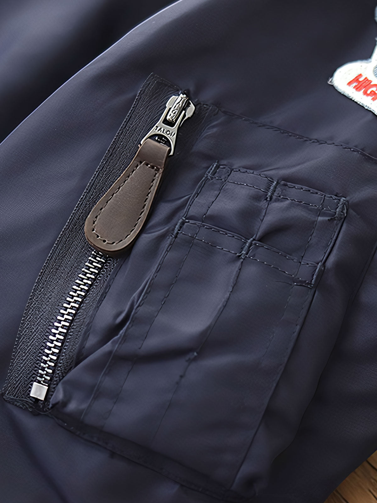 製品画像:ヴィンテージMA-1フライトジャケットの正面図。防水ナイロン素材とオレンジ色の裏地、刺繍バッジが特徴的なデザイン。
詳細画像:刺繍バッジと識別テープ、ジッパーのディテールをクローズアップした画像。ミリタリーウェアの本格的なスタイルを強調。