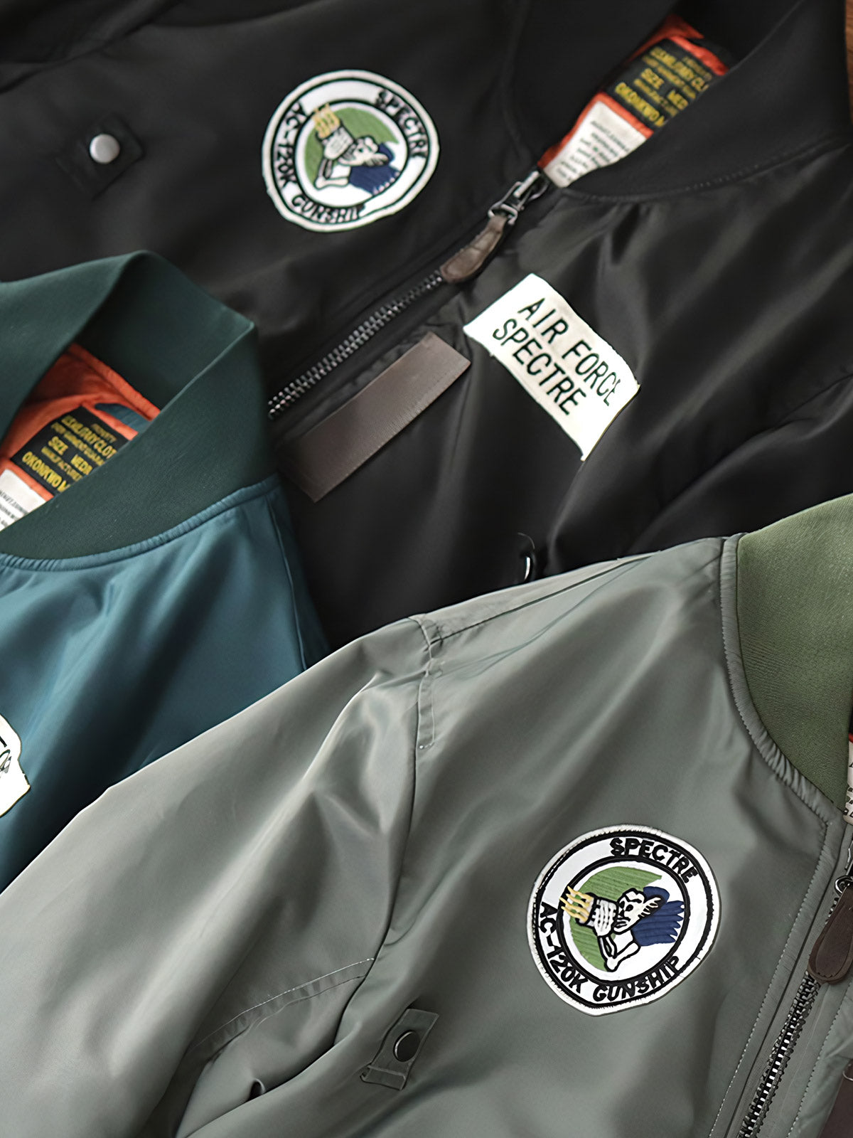 製品画像:ヴィンテージMA-1フライトジャケットの正面図。防水ナイロン素材とオレンジ色の裏地、刺繍バッジが特徴的なデザイン。
詳細画像:刺繍バッジと識別テープ、ジッパーのディテールをクローズアップした画像。ミリタリーウェアの本格的なスタイルを強調。