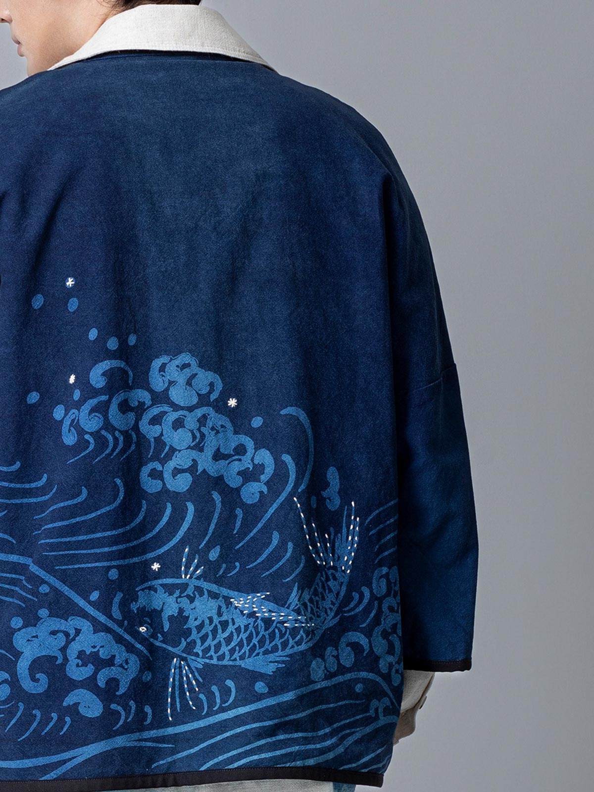 詳細画像:和柄の抜染と段落ち抜染のディテールをクローズアップ。刺し子刺繍と織り帯のディテールが、工芸的な価値を引き立てる。
モデル画像:モデルがリネンはんてんを着用。リネンパンツと合わせた品のあるカジュアルスタイルを提案。