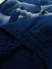 製品画像: 雲海柄藍染めバイカージャケット全体表示。ジャカードコットン素材と独特な抜染技法で、都会と自然が交わるデザイン。
詳細画像: 雲海抜染柄と伸縮性のある裾デザインのディテール表示。テクスチャーの深みと実用的な裾仕上げが際立つディテール。