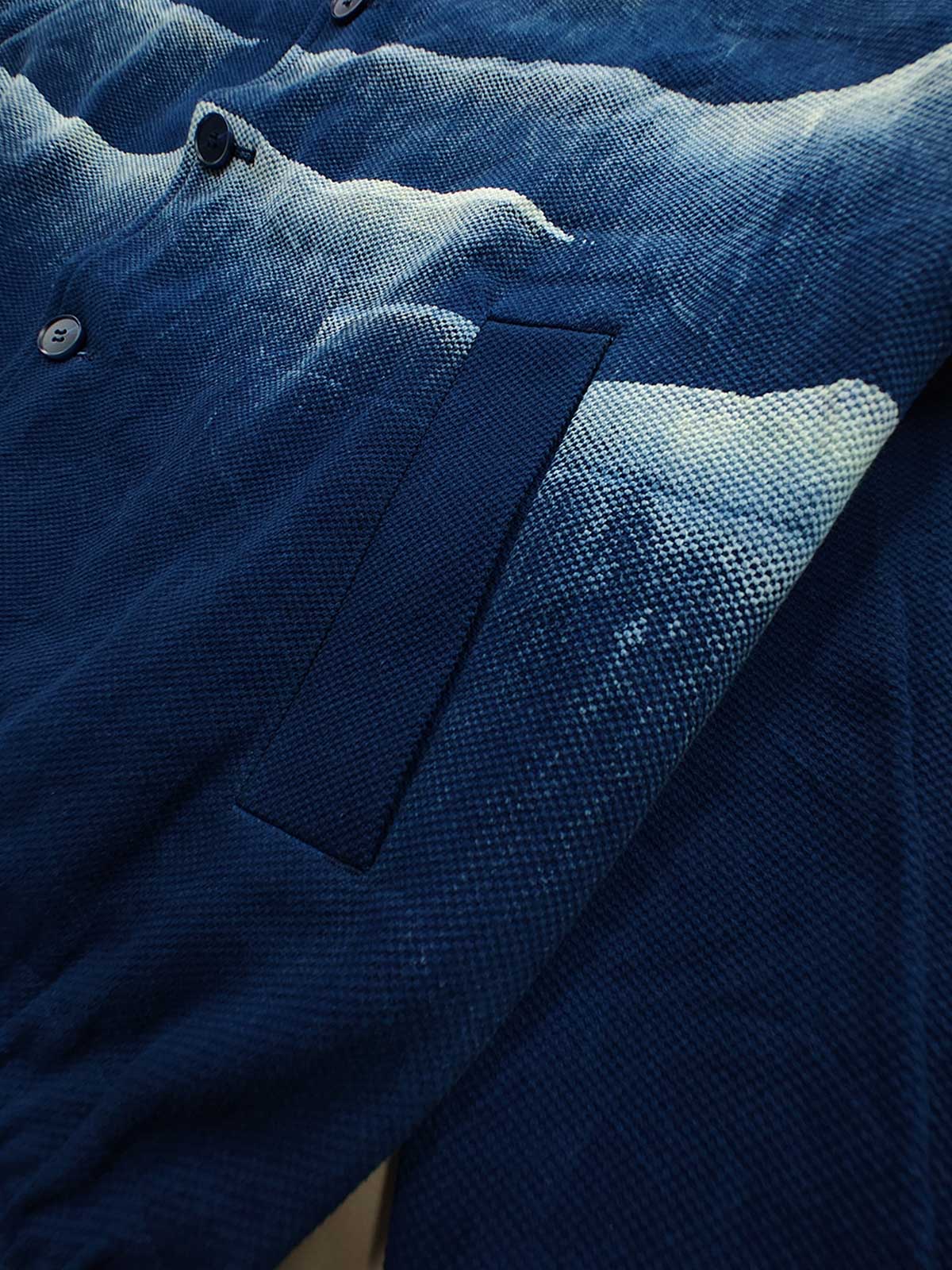 製品画像: 雲海柄藍染めバイカージャケット全体表示。ジャカードコットン素材と独特な抜染技法で、都会と自然が交わるデザイン。
詳細画像: 雲海抜染柄と伸縮性のある裾デザインのディテール表示。テクスチャーの深みと実用的な裾仕上げが際立つディテール。