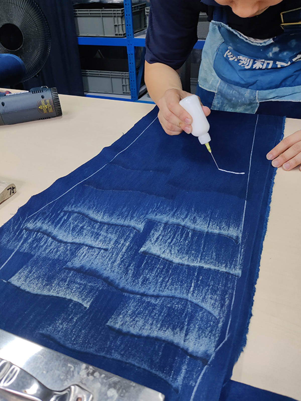 製品画像: 雲海柄藍染めバイカージャケット全体表示。ジャカードコットン素材と独特な抜染技法で、都会と自然が交わるデザイン。
詳細画像: 雲海抜染柄と伸縮性のある裾デザインのディテール表示。テクスチャーの深みと実用的な裾仕上げが際立つディテール。