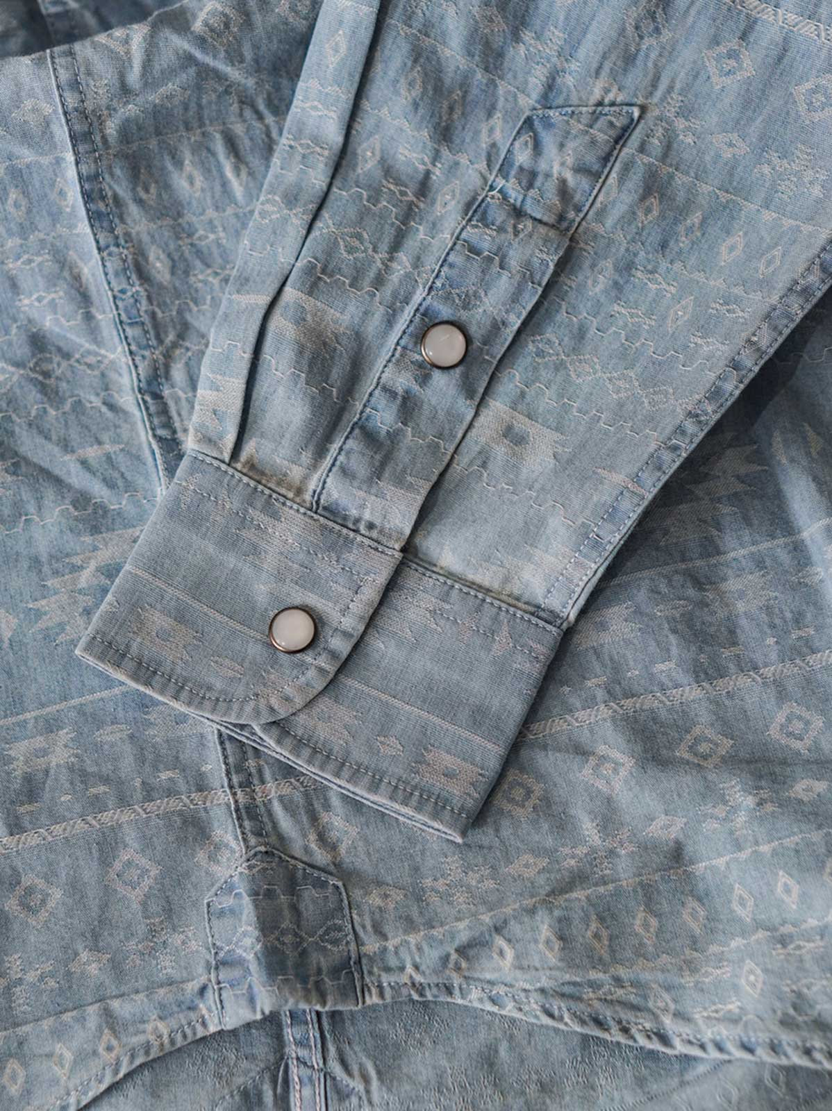 製品画像(全体展示):
ナバホ柄ジャガードデニムシャツの全体展示画像。バタフライ「蝶」、サン「太陽」、メディスンアイ「薬師の目」など、ナバホ文化を象徴するモチーフが施されたデザイン。
詳細画像(織り目とディテール):
ナバホ柄ジャガードデニムシャツの織り目とディテールを強調した画像。コットンとポリエステルの混合生地が耐摩耗性と通気性を提供する様子。