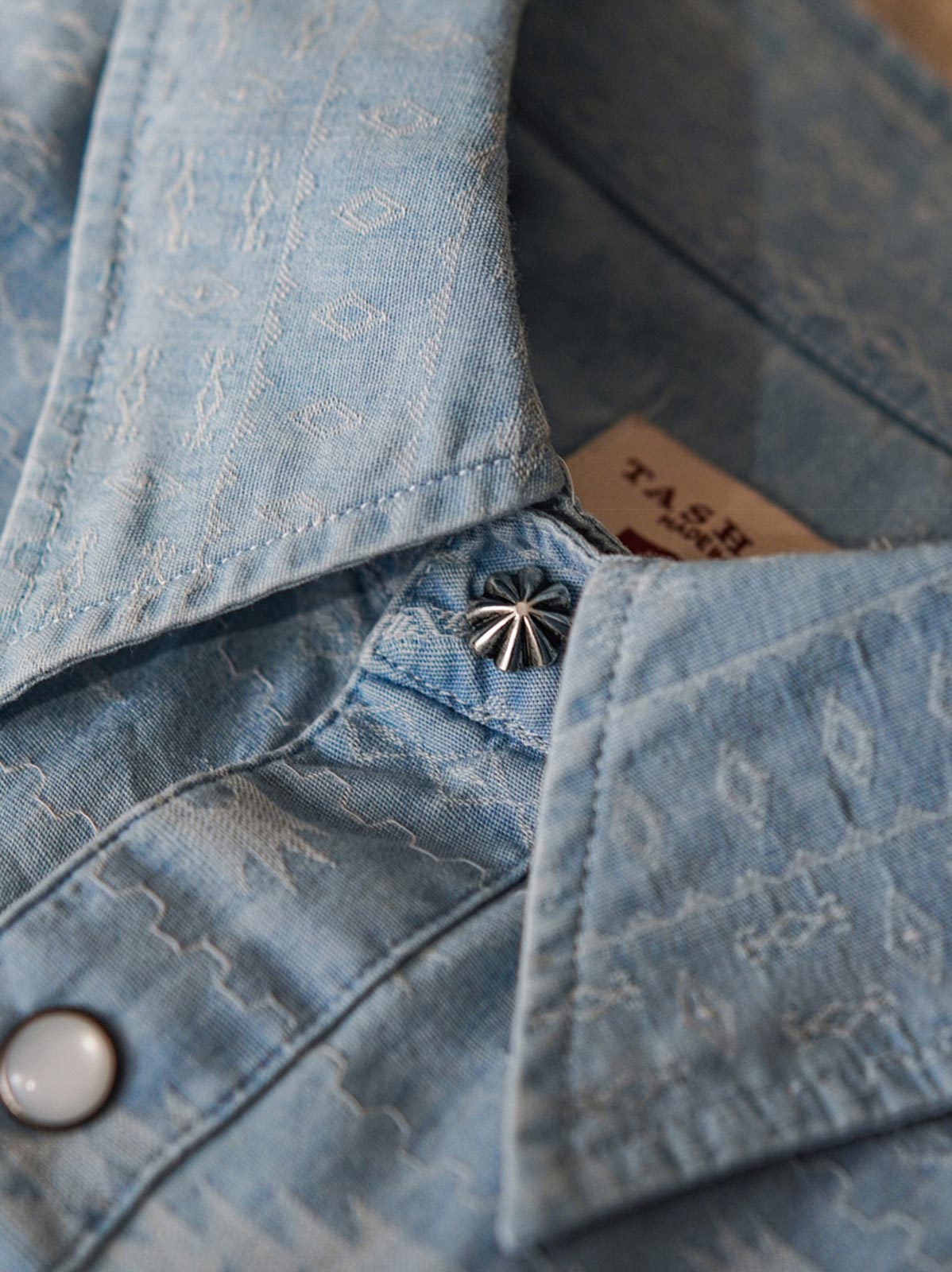 製品画像(全体展示):
ナバホ柄ジャガードデニムシャツの全体展示画像。バタフライ「蝶」、サン「太陽」、メディスンアイ「薬師の目」など、ナバホ文化を象徴するモチーフが施されたデザイン。
詳細画像(織り目とディテール):
ナバホ柄ジャガードデニムシャツの織り目とディテールを強調した画像。コットンとポリエステルの混合生地が耐摩耗性と通気性を提供する様子。