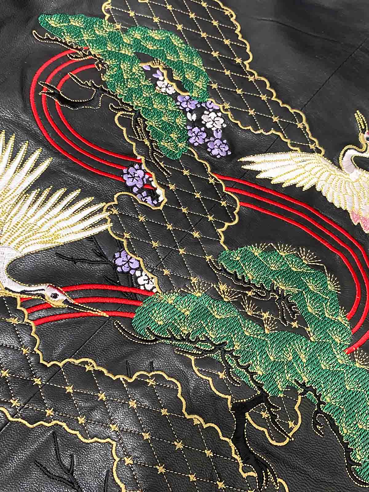 製品画像: 横須賀鶴図刺繍 羊革ジャケット全体画像、吉祥の象徴である「鶴図」刺繍と上質な輸入羊革のデザイン
詳細画像: 横須賀の伝統技法を用いた鶴、松、雲の刺繍ディテール、立体感ある精巧な工芸