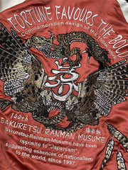 製品画像: リバーシブル シルク刺繍 横須賀 「Fortune Favors the Bold」(幸運は勇者を好む) ジャケットの全体画像、日本文化とヴィンテージスタイルの融合
詳細画像: 「Fortune Favors the Bold」(幸運は勇者を好む)の文字と鷹と蛇のトーテム、七福神の刺繍ディテール、横須賀刺繍の精緻な技法