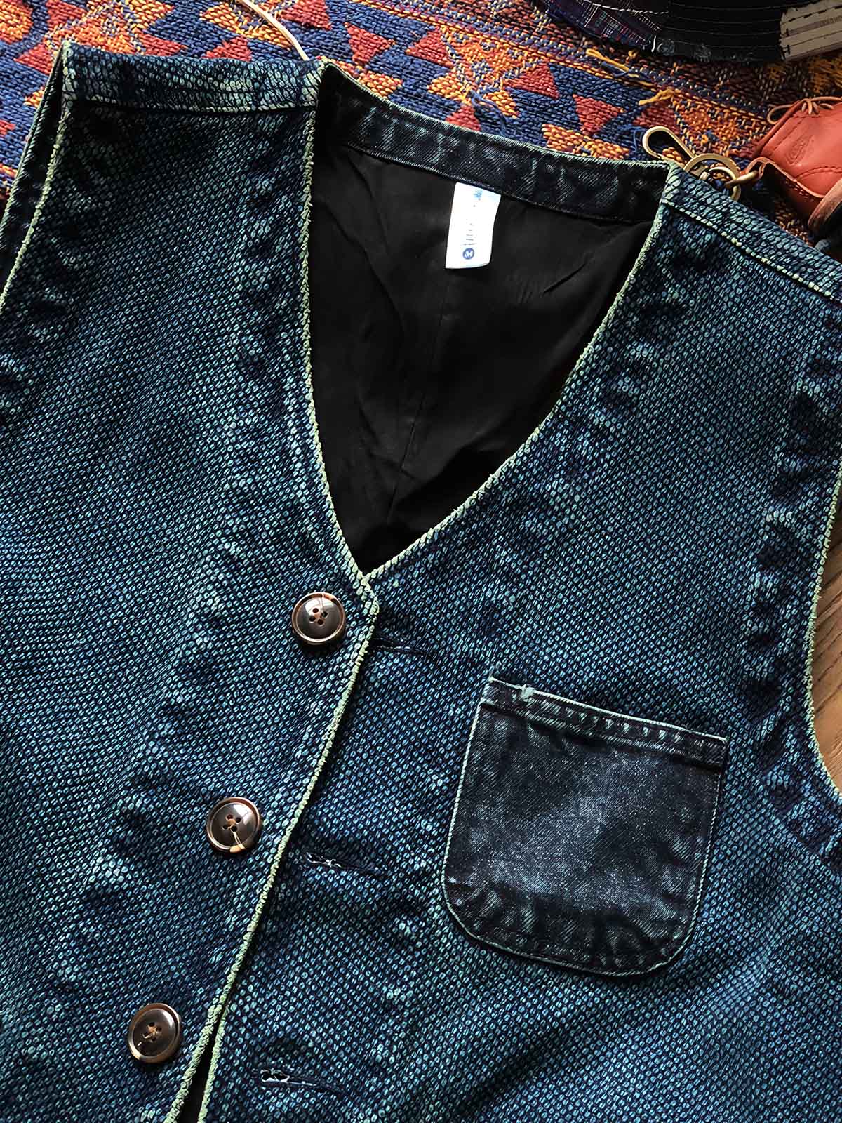 製品画像
剣道着風のデザインを取り入れた多ポケットワークベスト。植物藍染めで仕上げられ、日本武士文化を彷彿とさせるクラシックなスタイルが特徴。軽量なコットン素材を使用し、通勤やアウトドアに最適な正面図。
詳細画像
藍染めのディテールを特写した多ポケットワークベスト。牛角ボタンがアクセントとして使用され、レトロな雰囲気を演出。ポケット部分の縫製や植物藍染めの繊細な色合いが際立つ特写画像。