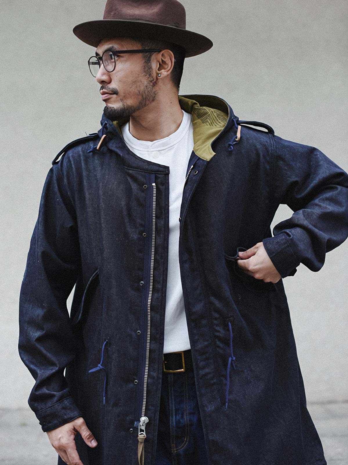 詳細画像: YKK製スナップボタンと特注シルバーカラージッパー、ブルー樹脂ボタンのディテールをクローズアップした画像。ヴィンテージ感を引き立てる丁寧なディテールが際立つ。
モデル画像: モデルがデニムバージョンのM51フィッシュテールコートを着用し、カーゴパンツとスニーカーを合わせたヴィンテージミリタリースタイルのコーディネート画像。軽やかさと保温性を両立した冬のデイリースタイルを提案。