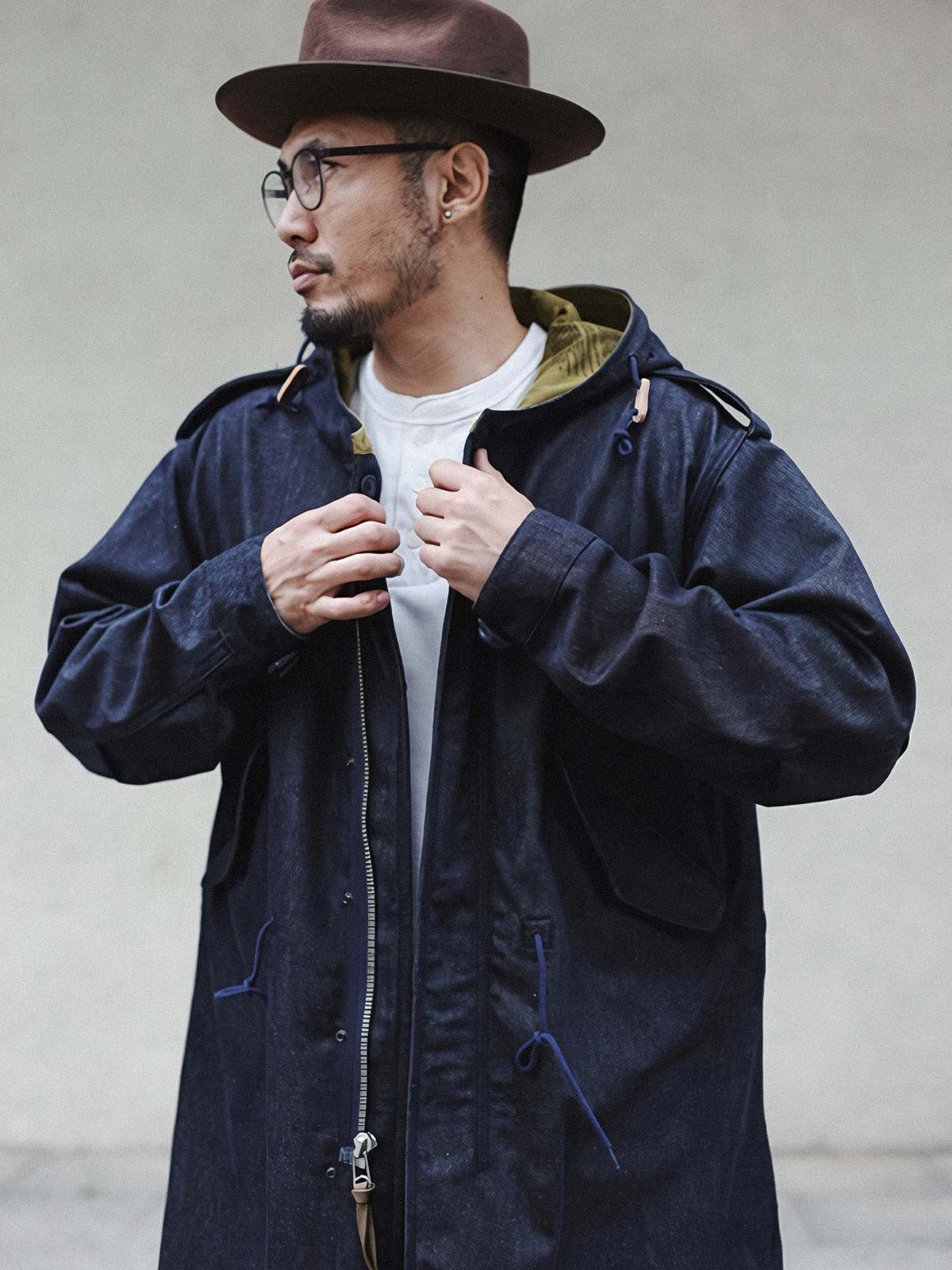 詳細画像: YKK製スナップボタンと特注シルバーカラージッパー、ブルー樹脂ボタンのディテールをクローズアップした画像。ヴィンテージ感を引き立てる丁寧なディテールが際立つ。
モデル画像: モデルがデニムバージョンのM51フィッシュテールコートを着用し、カーゴパンツとスニーカーを合わせたヴィンテージミリタリースタイルのコーディネート画像。軽やかさと保温性を両立した冬のデイリースタイルを提案。