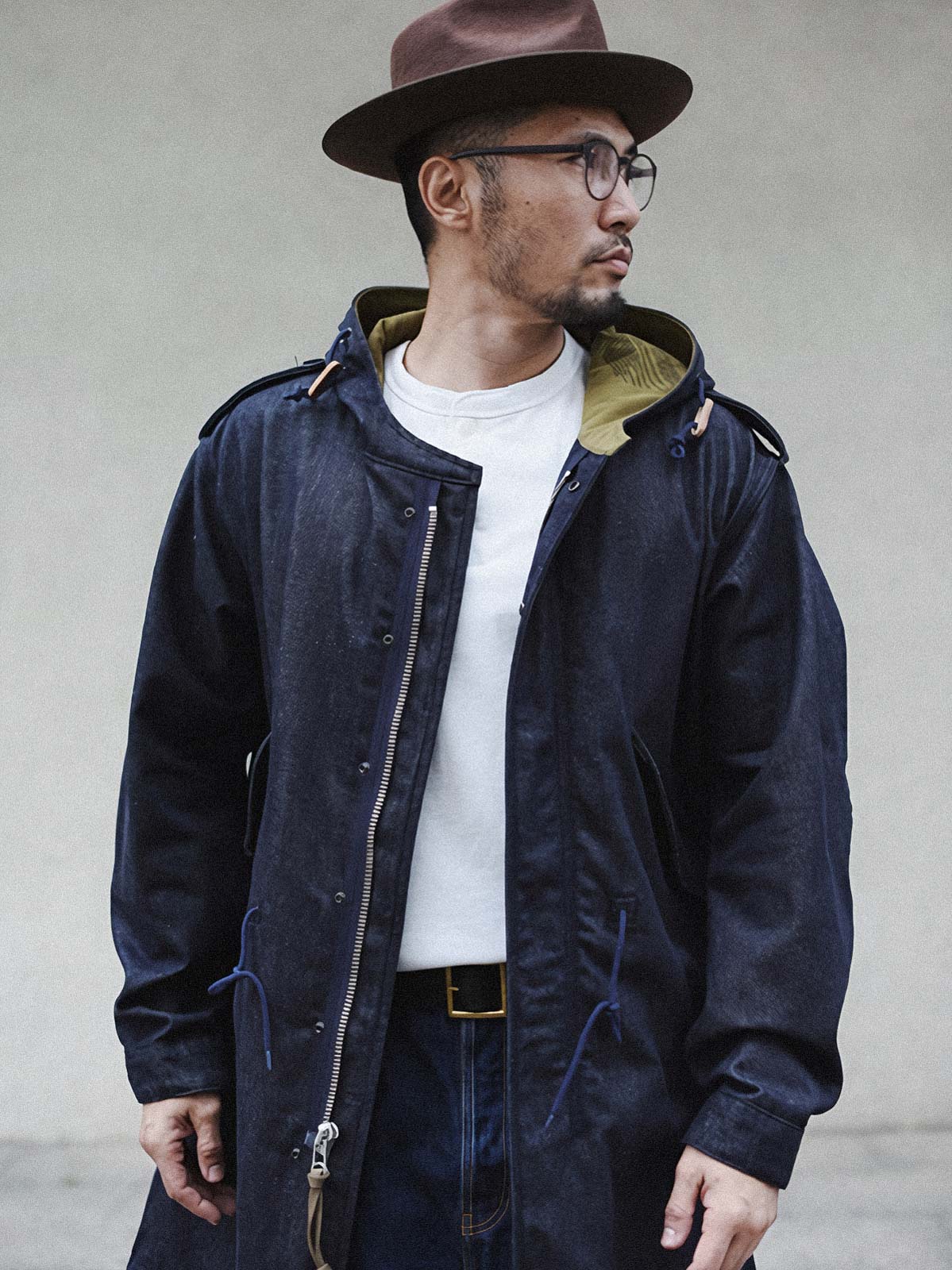 詳細画像: YKK製スナップボタンと特注シルバーカラージッパー、ブルー樹脂ボタンのディテールをクローズアップした画像。ヴィンテージ感を引き立てる丁寧なディテールが際立つ。
モデル画像: モデルがデニムバージョンのM51フィッシュテールコートを着用し、カーゴパンツとスニーカーを合わせたヴィンテージミリタリースタイルのコーディネート画像。軽やかさと保温性を両立した冬のデイリースタイルを提案。