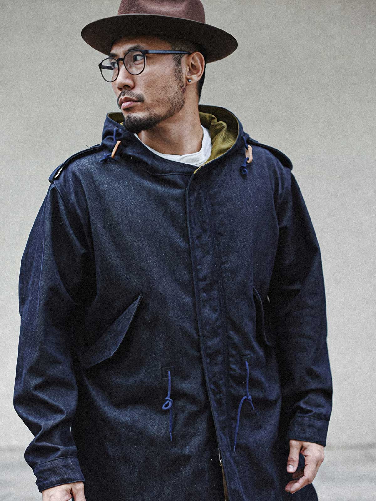 詳細画像: YKK製スナップボタンと特注シルバーカラージッパー、ブルー樹脂ボタンのディテールをクローズアップした画像。ヴィンテージ感を引き立てる丁寧なディテールが際立つ。
モデル画像: モデルがデニムバージョンのM51フィッシュテールコートを着用し、カーゴパンツとスニーカーを合わせたヴィンテージミリタリースタイルのコーディネート画像。軽やかさと保温性を両立した冬のデイリースタイルを提案。