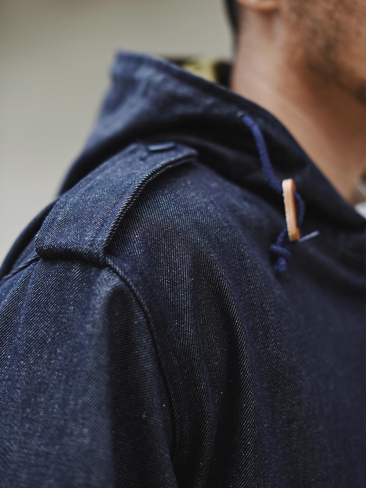 詳細画像: YKK製スナップボタンと特注シルバーカラージッパー、ブルー樹脂ボタンのディテールをクローズアップした画像。ヴィンテージ感を引き立てる丁寧なディテールが際立つ。
モデル画像: モデルがデニムバージョンのM51フィッシュテールコートを着用し、カーゴパンツとスニーカーを合わせたヴィンテージミリタリースタイルのコーディネート画像。軽やかさと保温性を両立した冬のデイリースタイルを提案。