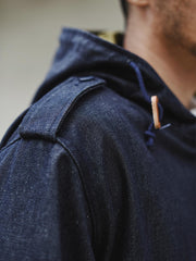 詳細画像: YKK製スナップボタンと特注シルバーカラージッパー、ブルー樹脂ボタンのディテールをクローズアップした画像。ヴィンテージ感を引き立てる丁寧なディテールが際立つ。
モデル画像: モデルがデニムバージョンのM51フィッシュテールコートを着用し、カーゴパンツとスニーカーを合わせたヴィンテージミリタリースタイルのコーディネート画像。軽やかさと保温性を両立した冬のデイリースタイルを提案。