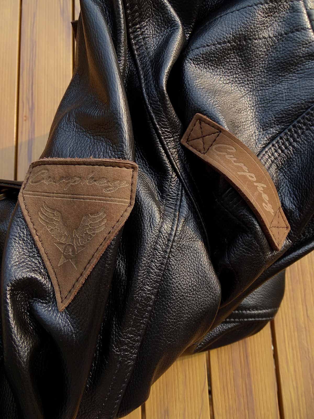 製品画像: 9ポケットフィールドフード付きフルグレインレザージャケット全体イメージ画像。黒いシボ加工レザーとヴィンテージ感漂うオイル仕上げのスエードディテールが特徴で、アウトドアやバイクライドにも適した多機能デザイン。
詳細画像: YKKアンティークブロンズジッパーとオイルドスエードレザーの補強ディテールをクローズアップした画像。耐久性とクラシックな風合いが際立つ仕上がり。