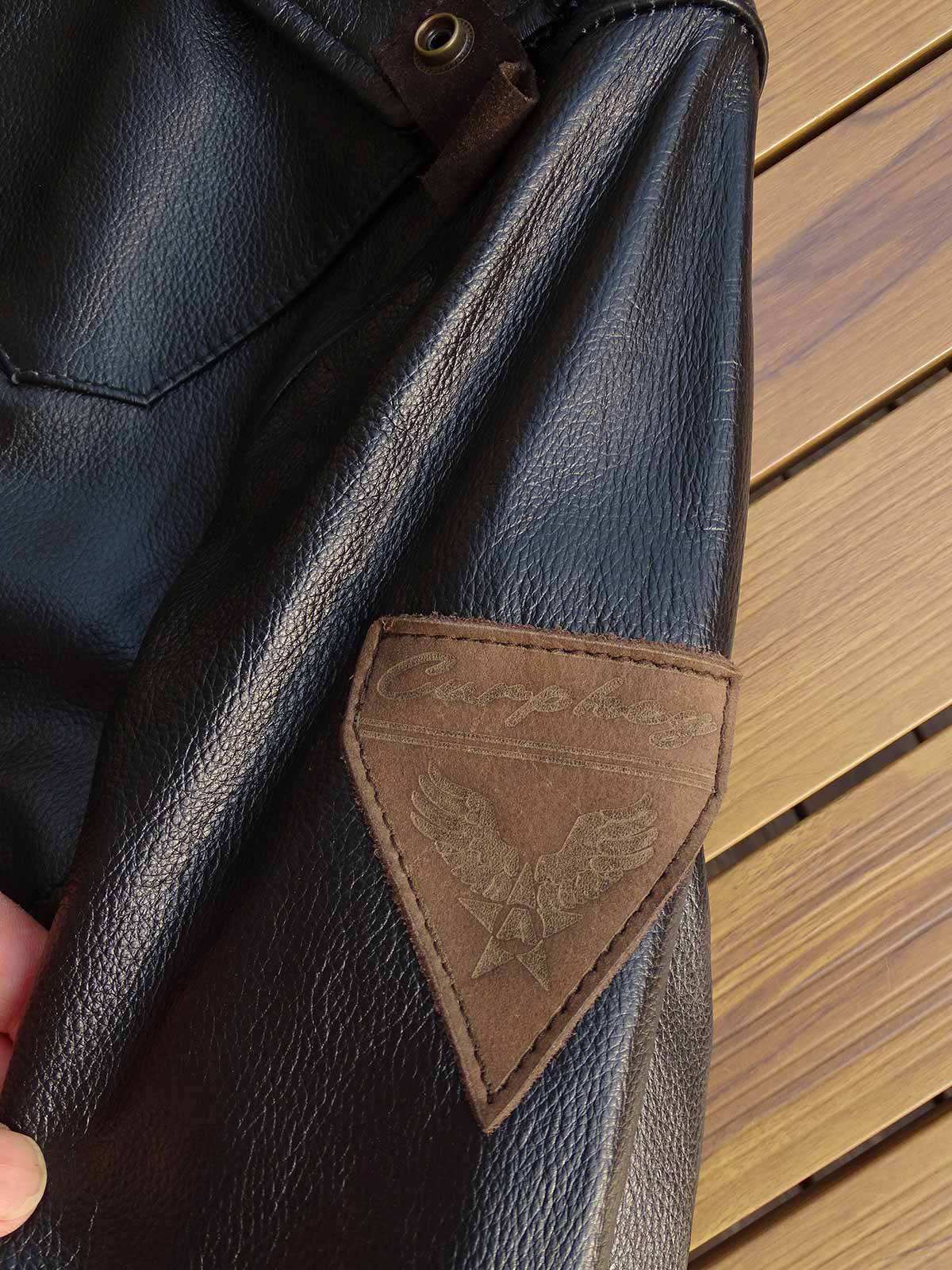 製品画像: 9ポケットフィールドフード付きフルグレインレザージャケット全体イメージ画像。黒いシボ加工レザーとヴィンテージ感漂うオイル仕上げのスエードディテールが特徴で、アウトドアやバイクライドにも適した多機能デザイン。
詳細画像: YKKアンティークブロンズジッパーとオイルドスエードレザーの補強ディテールをクローズアップした画像。耐久性とクラシックな風合いが際立つ仕上がり。