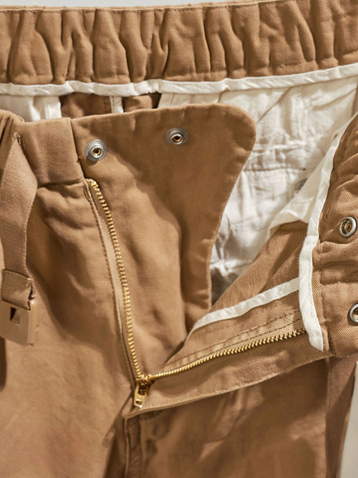 製品画像:紫タグが付いたワーク テーパードパンツの全体像。高品質な純銅YKKジッパーや金属ボタン、そしてしっかりとしたテーパードシルエットが際立ち、スタイリッシュで実用的なデザインが特徴のパンツを全体的に見せる展示画像。
詳細画像:紫タグが強調されたバックルベルトと隠しワークポケットのディテールクローズアップ。バックルベルト部分の調節機能と隠しポケットのディテールが、実用性とデザイン性を兼ね備えた特徴を詳しく見せる画像。