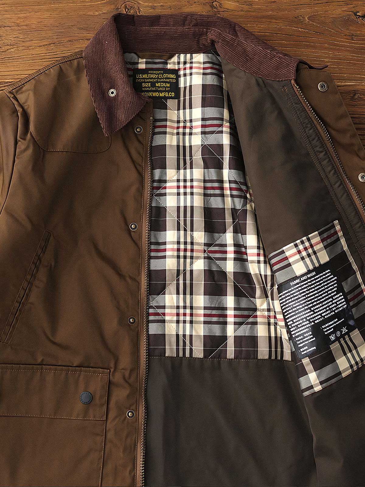 製品画像: コーデュロイカラーのコントラスト襟とオイルワックス加工が施されたハンティングジャケット。高密度梭織生地を使用し、耐久性とレトロ感を兼ね備えたデザイン。
詳細画像: チェック柄のキルティングライニングとスナップボタン付き風防襟のディテール。YKKのダブルヘッドラウンドリングジッパーと多機能ポケット配置が実用性を高めています。