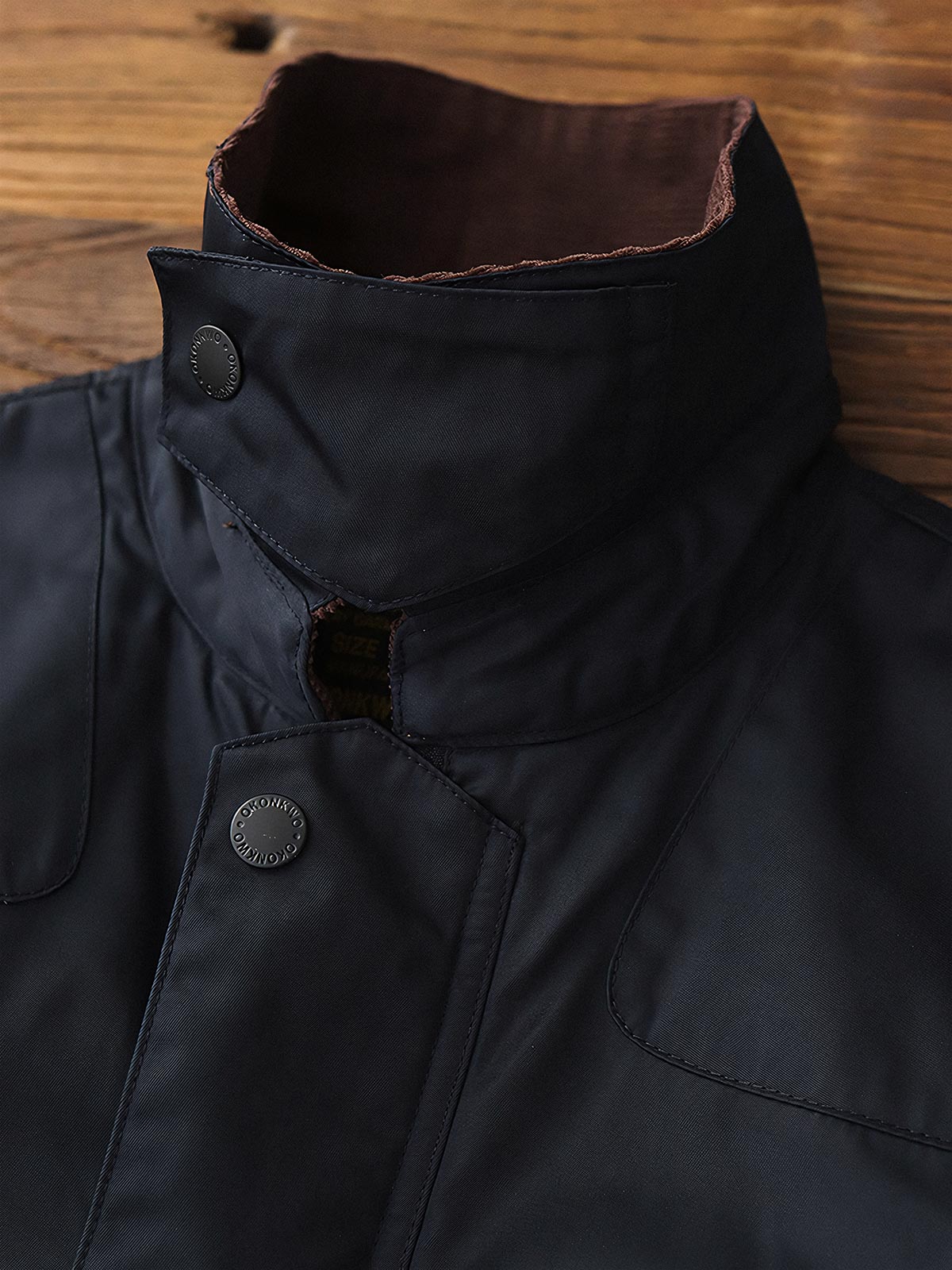 製品画像: コーデュロイカラーのコントラスト襟とオイルワックス加工が施されたハンティングジャケット。高密度梭織生地を使用し、耐久性とレトロ感を兼ね備えたデザイン。
詳細画像: チェック柄のキルティングライニングとスナップボタン付き風防襟のディテール。YKKのダブルヘッドラウンドリングジッパーと多機能ポケット配置が実用性を高めています。