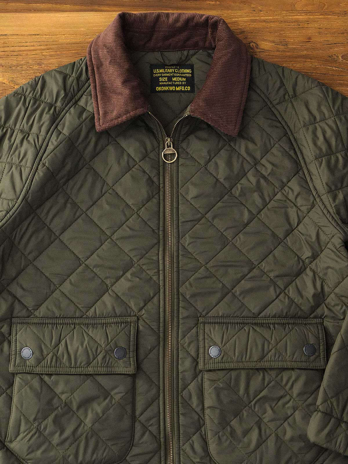 製品画像: ヴィンテージダイヤキルト中綿ジャケット正面展示図。クラシックなダイヤキルト縫製とコーデュロイ襟が特徴的なデザイン。軽量で暖かく、スリムなシルエット。
詳細画像: TALONの真鍮ジッパー、ラグランスリーブのディテール。大きなサイドポケットと斜めの隠しポケットが実用的なデザイン。