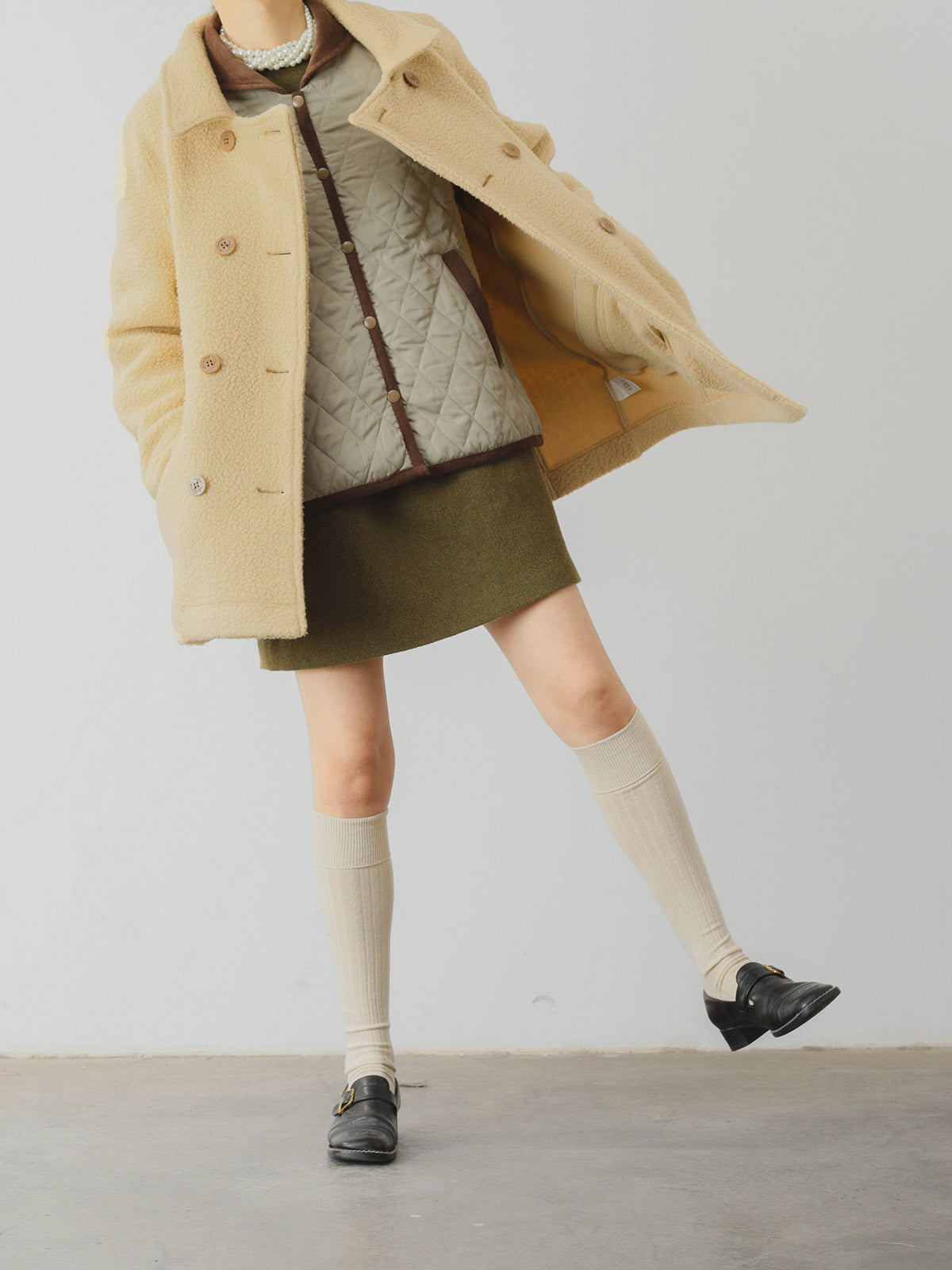 詳細画像: ツートーンのダイヤ柄キルティング加工が施されたコート、ポリエステル素材で軽量かつ耐久性のあるデザイン、ディテールにこだわったアクセント。
モデル画像: スカートやパンツとのコーディネートでイギリス風スクールスタイルを演出したモデルが着用したピーターパンカラーコート。