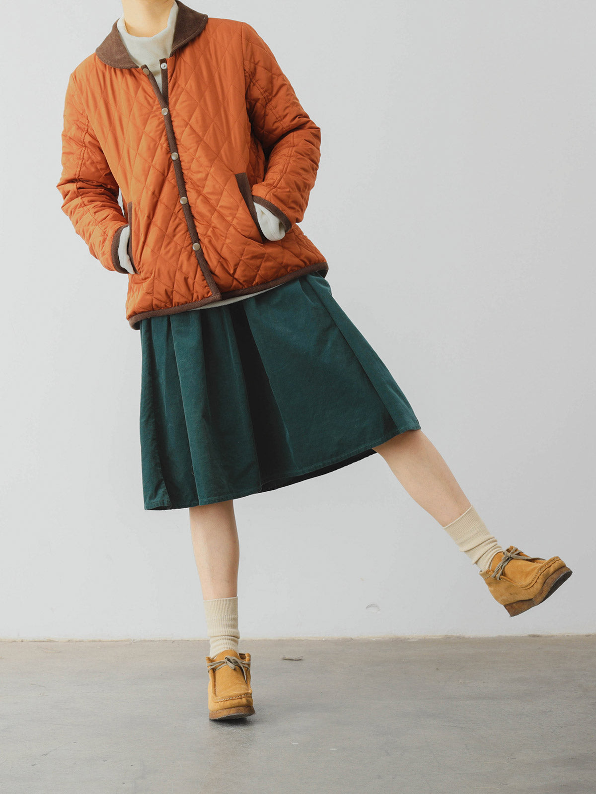 詳細画像: ツートーンのダイヤ柄キルティング加工が施されたコート、ポリエステル素材で軽量かつ耐久性のあるデザイン、ディテールにこだわったアクセント。
モデル画像: スカートやパンツとのコーディネートでイギリス風スクールスタイルを演出したモデルが着用したピーターパンカラーコート。