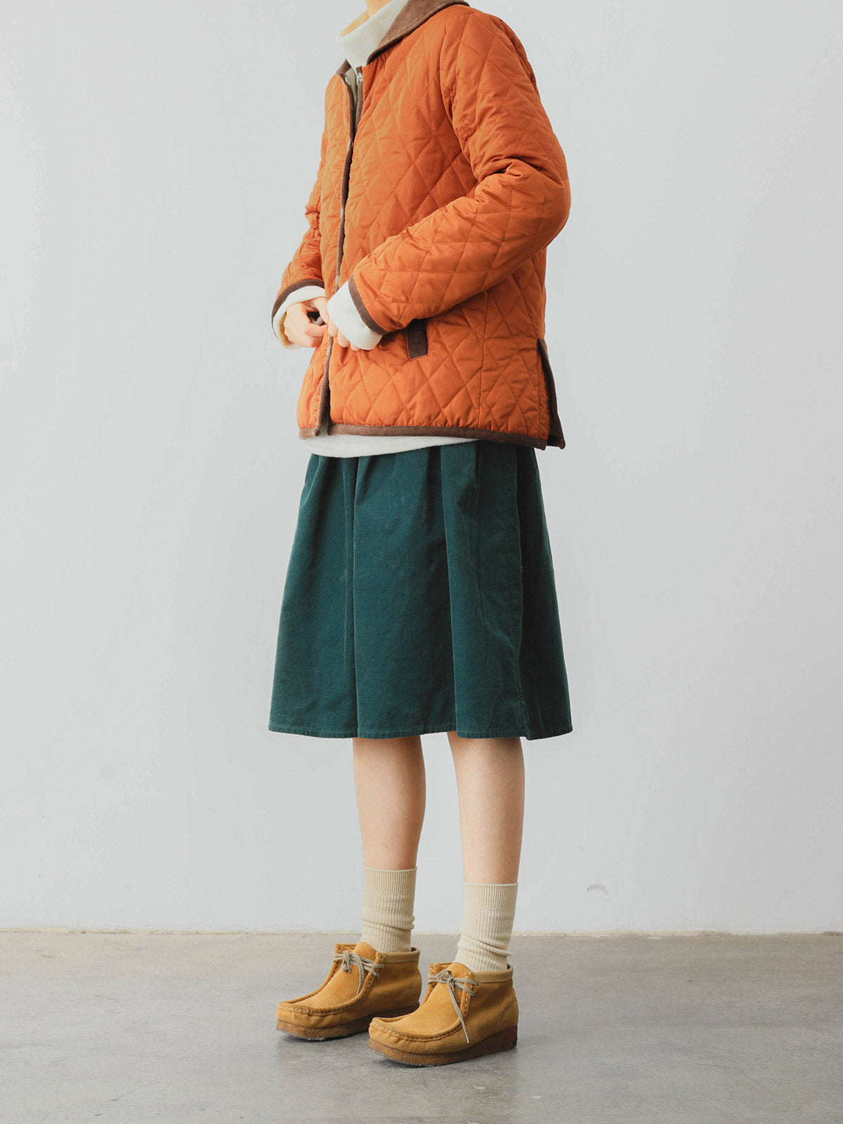 詳細画像: ツートーンのダイヤ柄キルティング加工が施されたコート、ポリエステル素材で軽量かつ耐久性のあるデザイン、ディテールにこだわったアクセント。
モデル画像: スカートやパンツとのコーディネートでイギリス風スクールスタイルを演出したモデルが着用したピーターパンカラーコート。