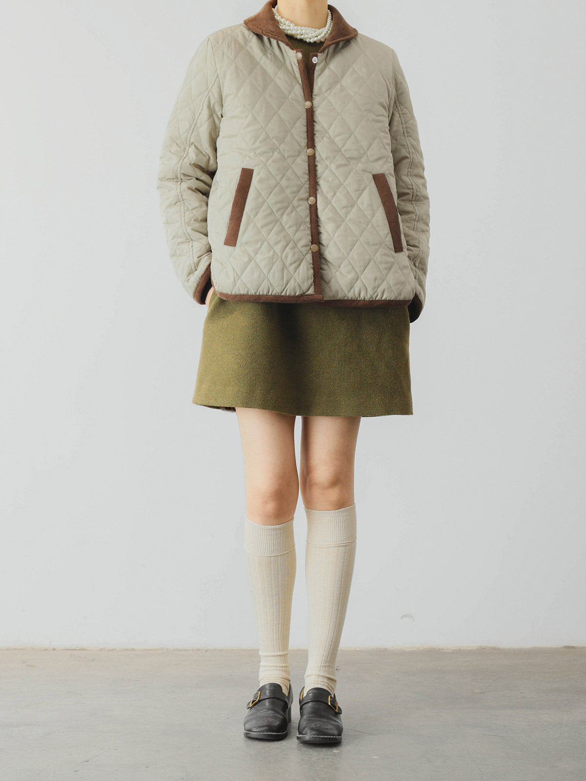 詳細画像: ツートーンのダイヤ柄キルティング加工が施されたコート、ポリエステル素材で軽量かつ耐久性のあるデザイン、ディテールにこだわったアクセント。
モデル画像: スカートやパンツとのコーディネートでイギリス風スクールスタイルを演出したモデルが着用したピーターパンカラーコート。